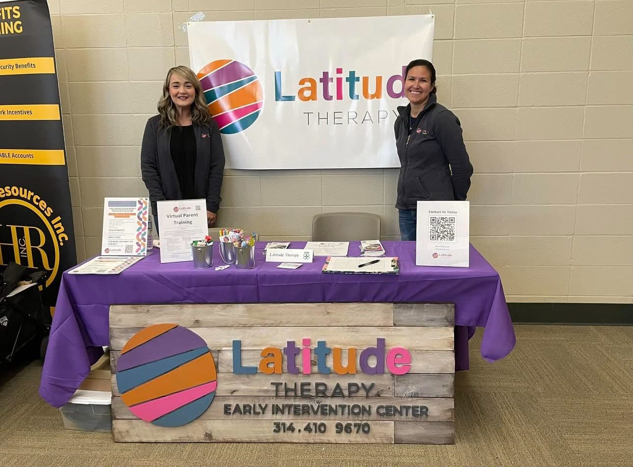 Two Latitude Therapy team members at an information table with the Latitude Therapy Early Intervention Center banner