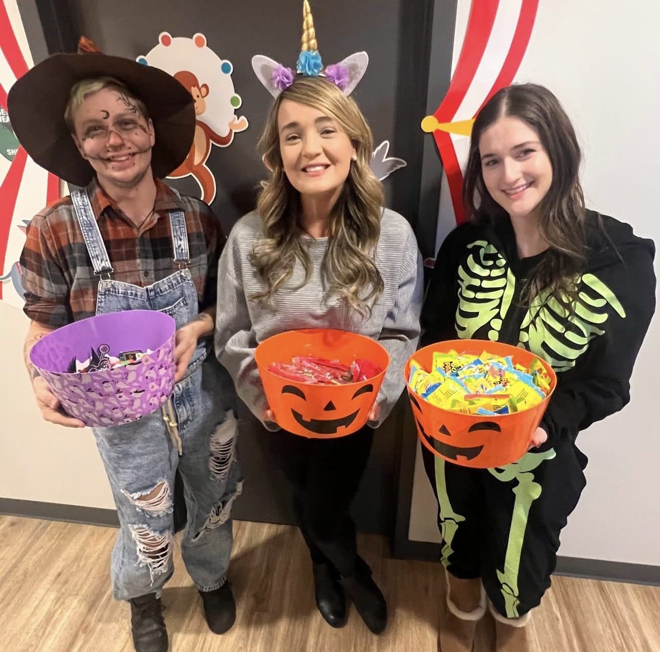Three Latitude Therapy team members in Halloween costumes holding candy bowls