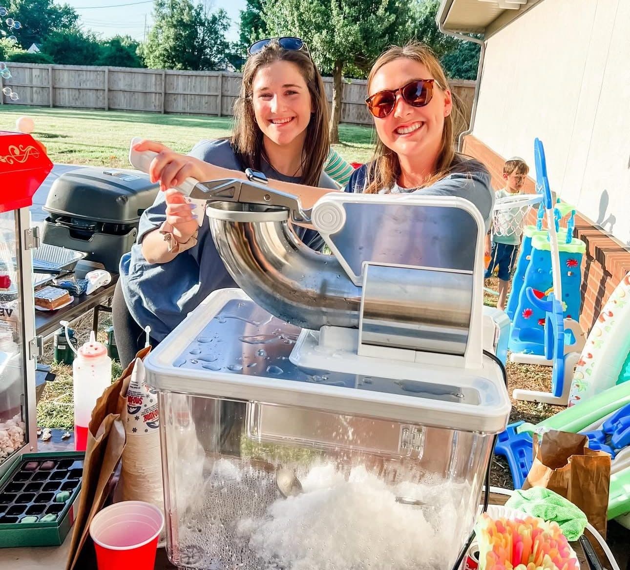 Two Latitude Therapy team members running a snow cone machine outdoors
