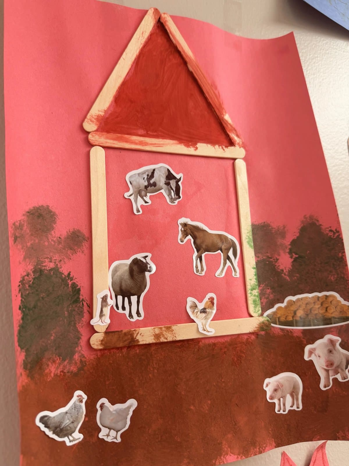 A finished craft-stick barn with farm animal stickers on red paper at Latitude's St. Peters center