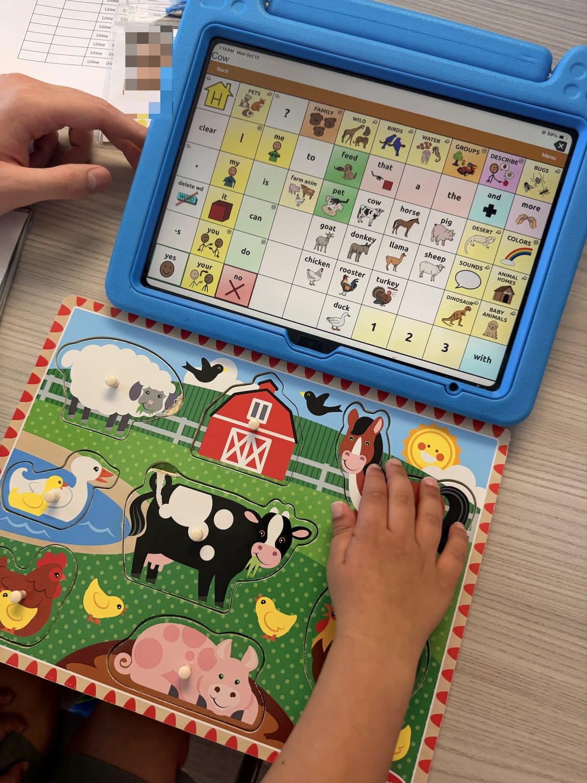 A child's hand on a farm animal puzzle next to a tablet with picture symbols at Latitude's St. Peters center