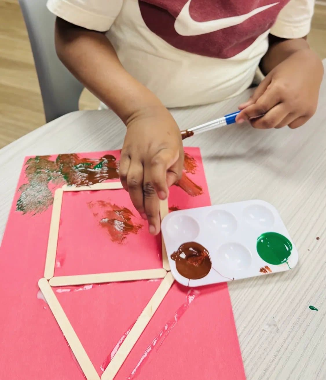 A child painting a craft-stick barn with a brush and paint palette at Latitude's St. Peters center